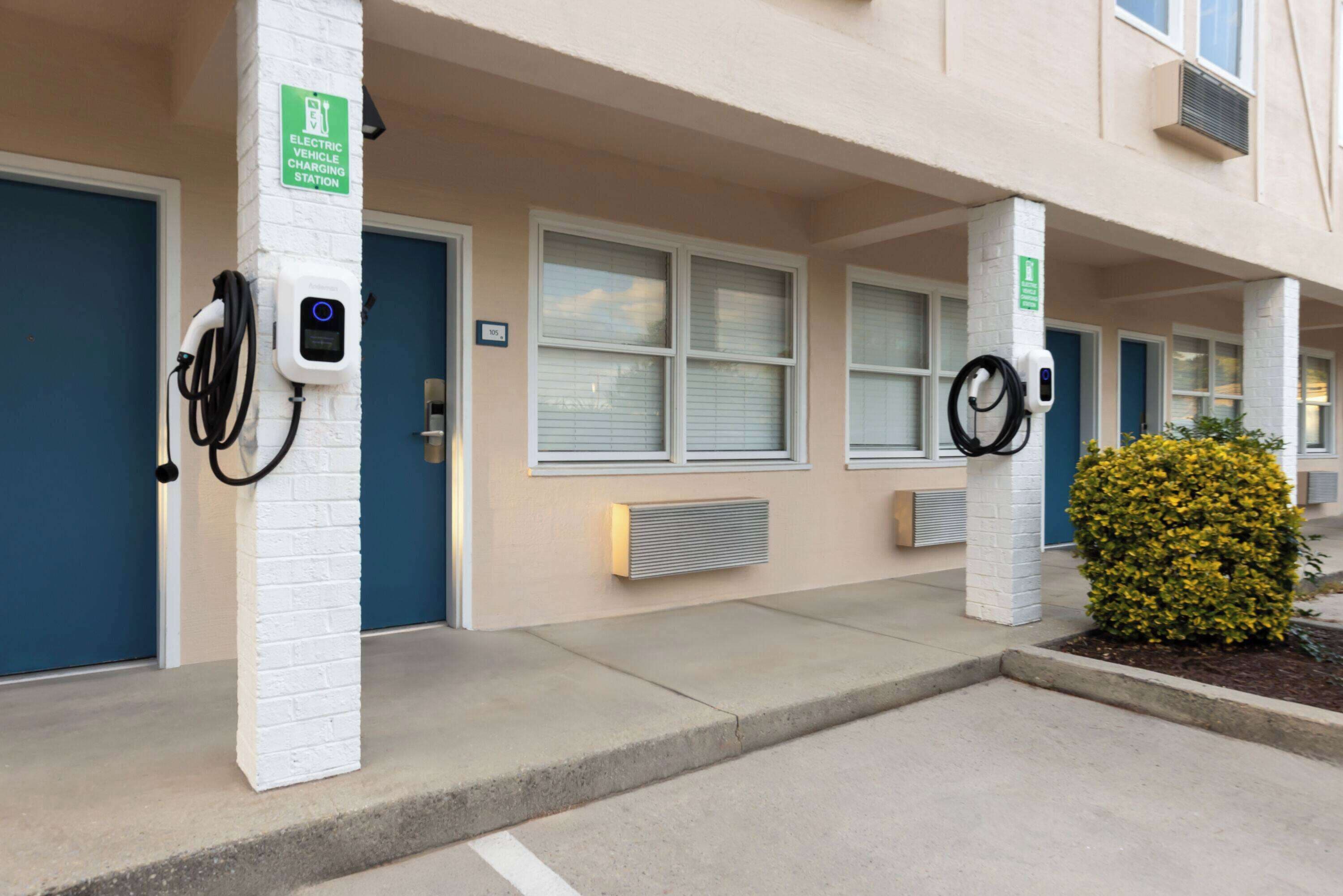 Un bâtiment doté de bornes de recharge pour véhicules électriques, une porte bleue et un petit arbuste jaune.