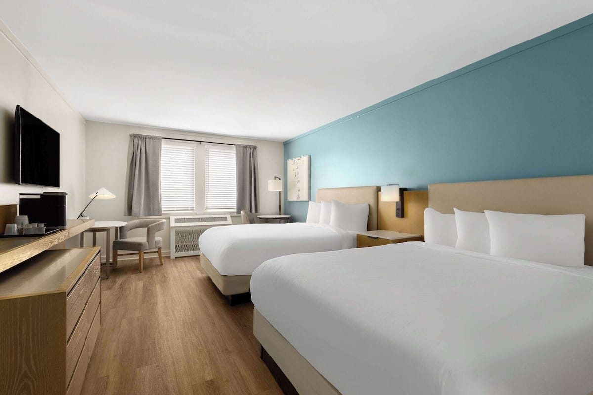 Habitación de hotel con dos camas, un escritorio, una silla, un televisor y una ventana con cortinas.
