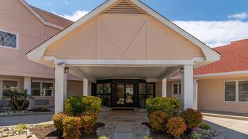 A building with a covered entrance, a triangular roof, and a landscaped front yard with shrubs and small plants.