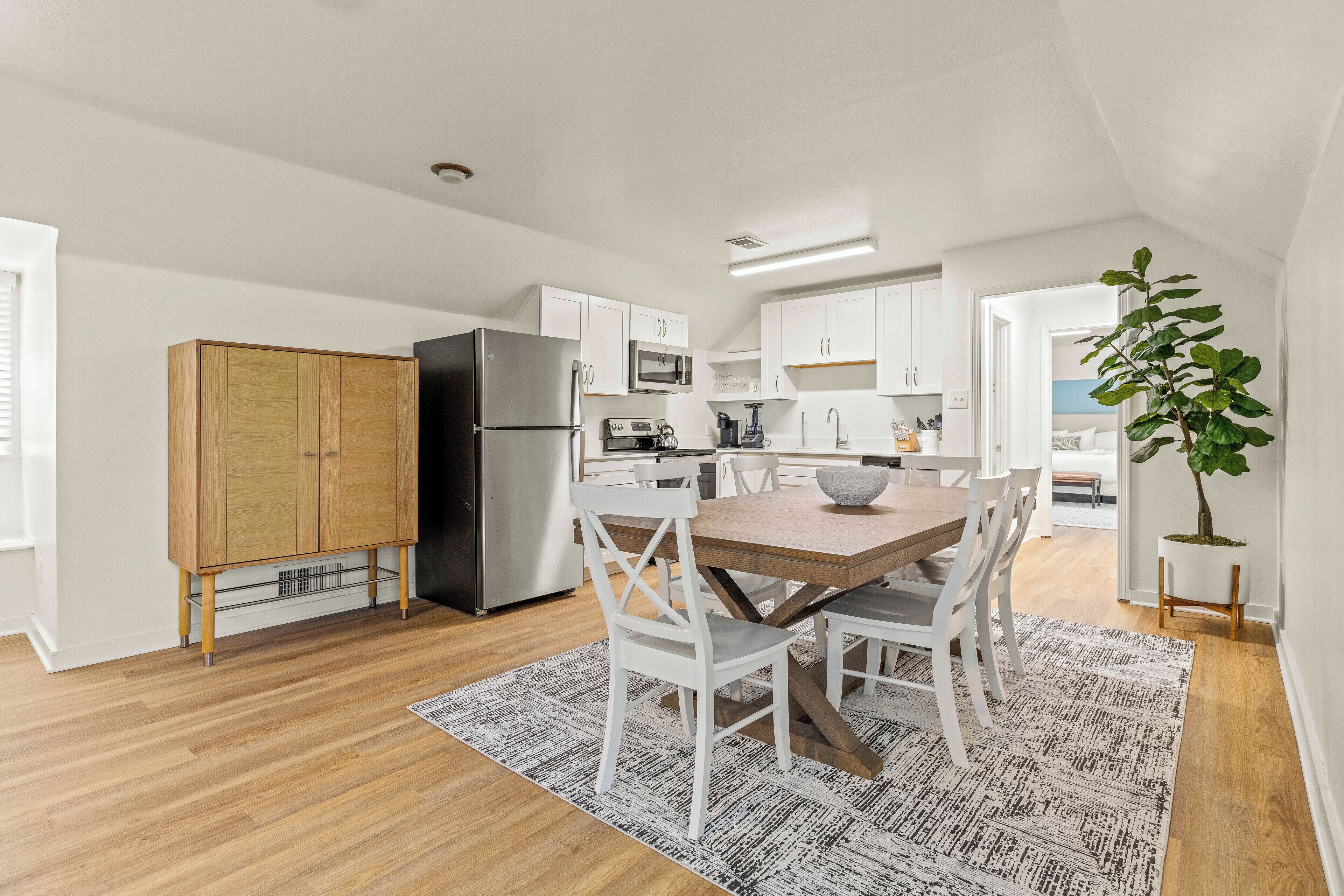 A modern kitchen with white cabinets, a black refrigerator, and a dining area with a wooden table and white chairs.