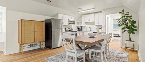A modern kitchen with white cabinets, a black refrigerator, and a dining area with a wooden table and white chairs.