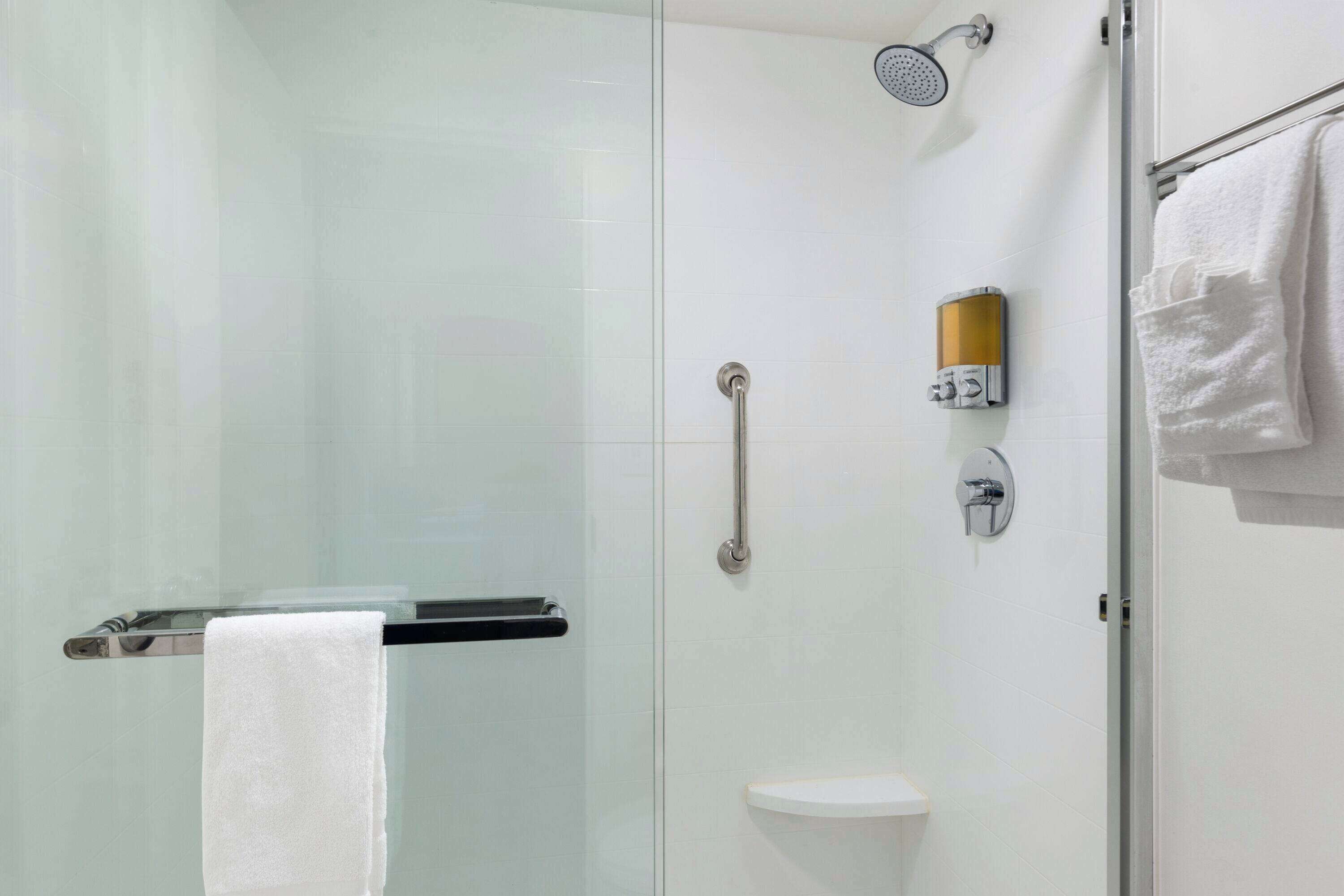 A modern bathroom with a glass shower enclosure, a handheld showerhead, a handheld shower control, a toilet, and a towel rack with a white towel.