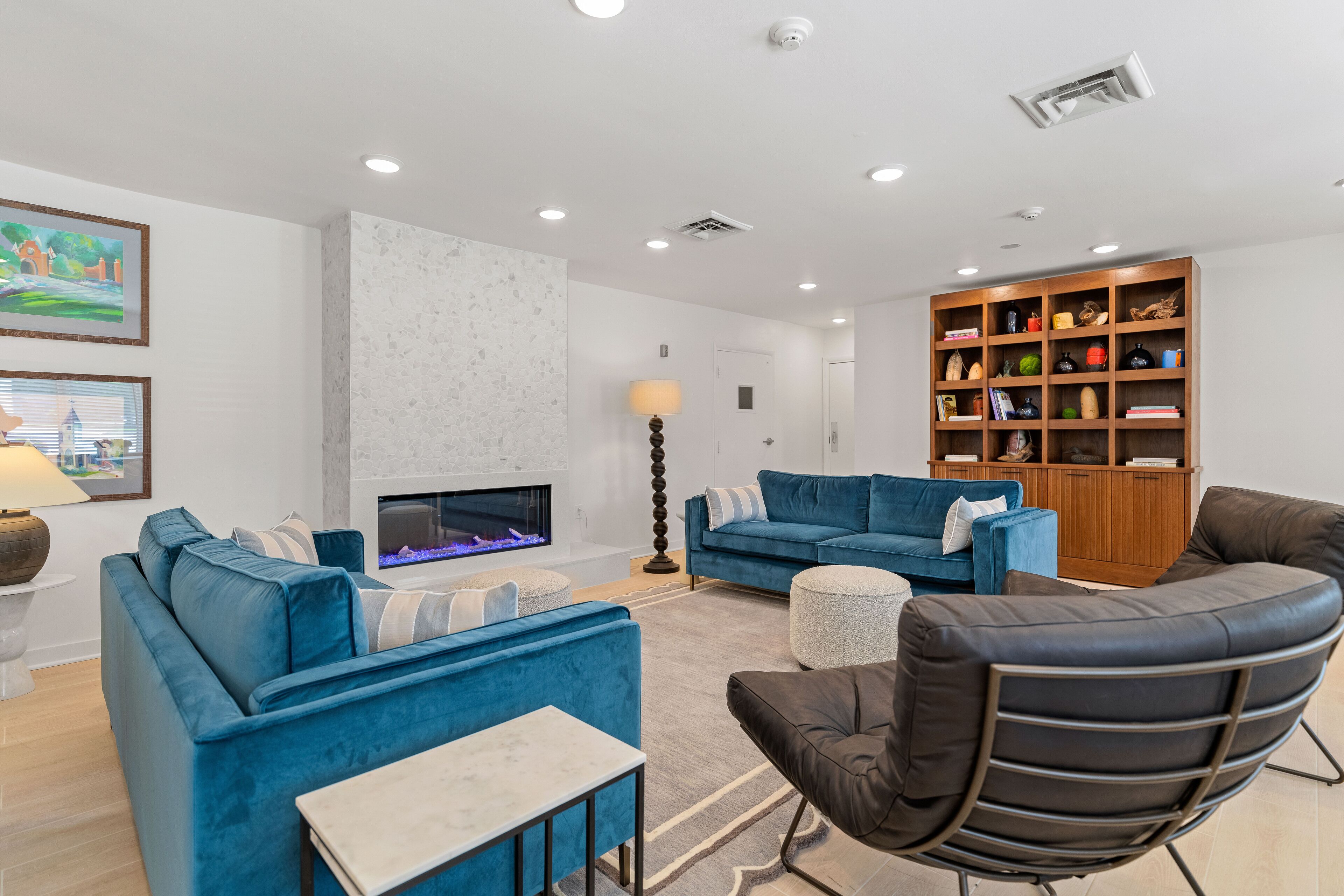 Una sala de estar moderna con chimenea, sofás azules, un sillón de cuero negro y una estantería de madera.