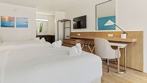 Habitación de hotel con dos camas, un escritorio, una silla, un televisor y obras de arte en las paredes.