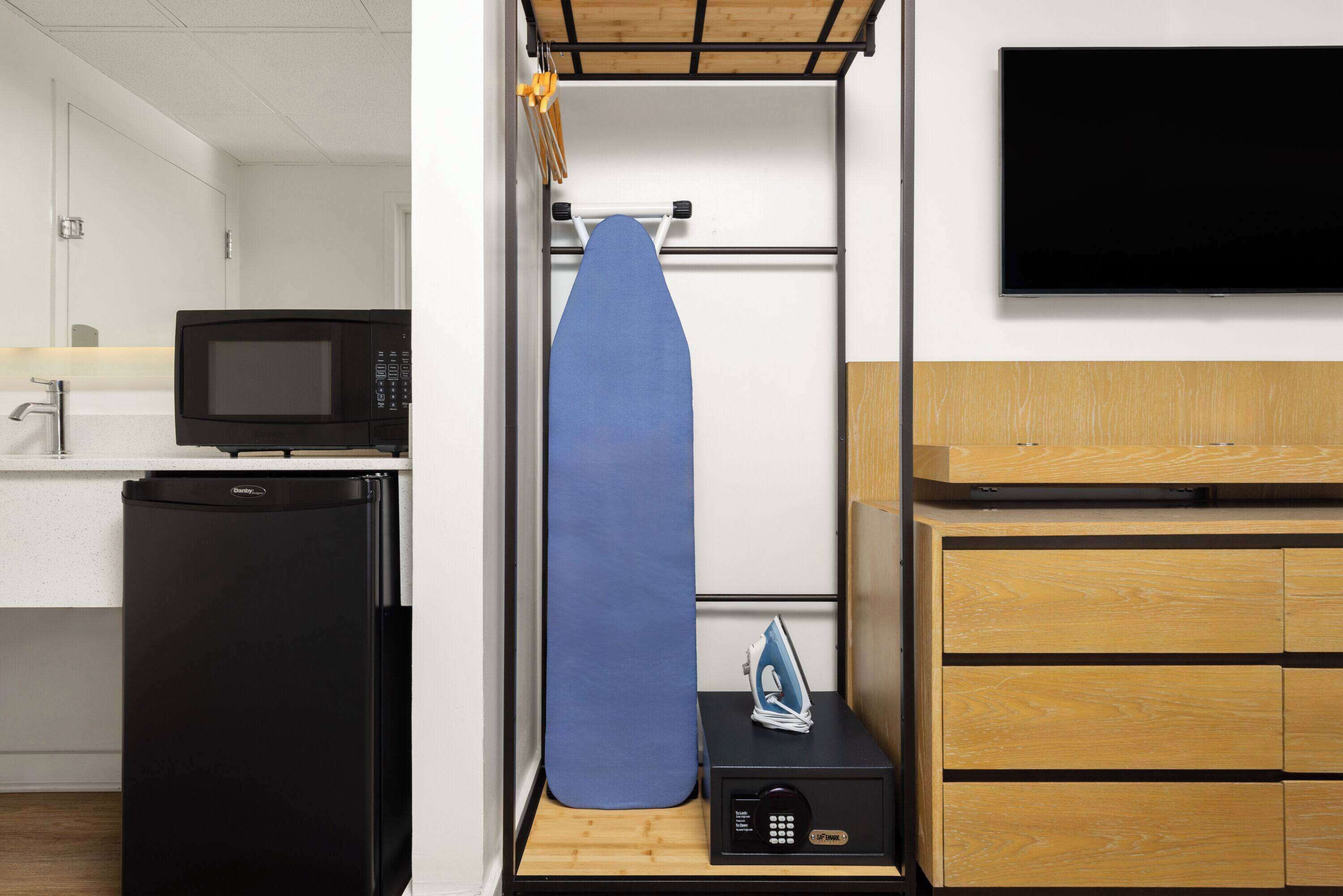 Una kitchenette compacta con microondas, un refrigerador pequeño y un mueble de madera con cajones.