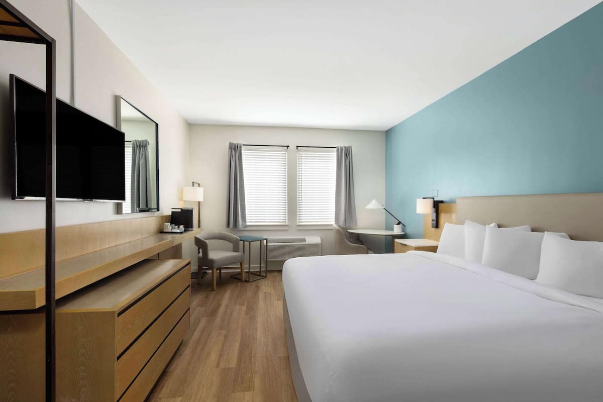 Habitación de hotel con una cama grande, un escritorio, una silla, un televisor y una ventana con cortinas.