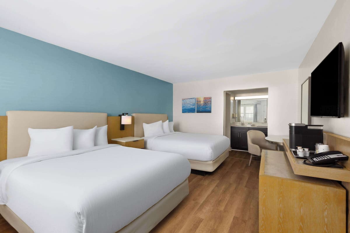 Una habitación de hotel con dos camas, un escritorio, una silla, cafetera y televisión.