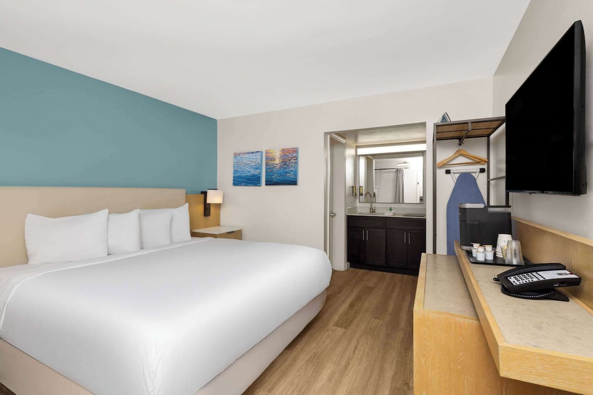 Habitación de hotel con una cama grande, un escritorio con teléfono, un espejo y un televisor.