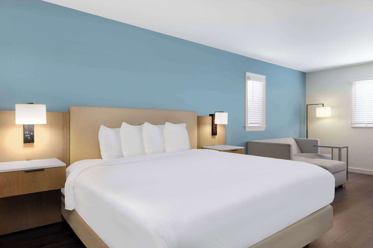 Una habitación de hotel con una cama grande, dos mesitas de noche, una silla y dos lámparas de pared.
