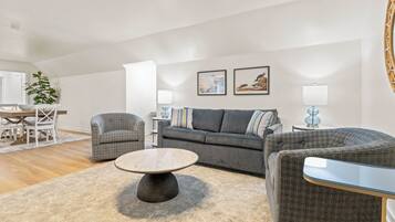 Un salon moderne avec un canapé gris, deux fauteuils, une table basse et un coin repas comprenant une table et des chaises blanches.