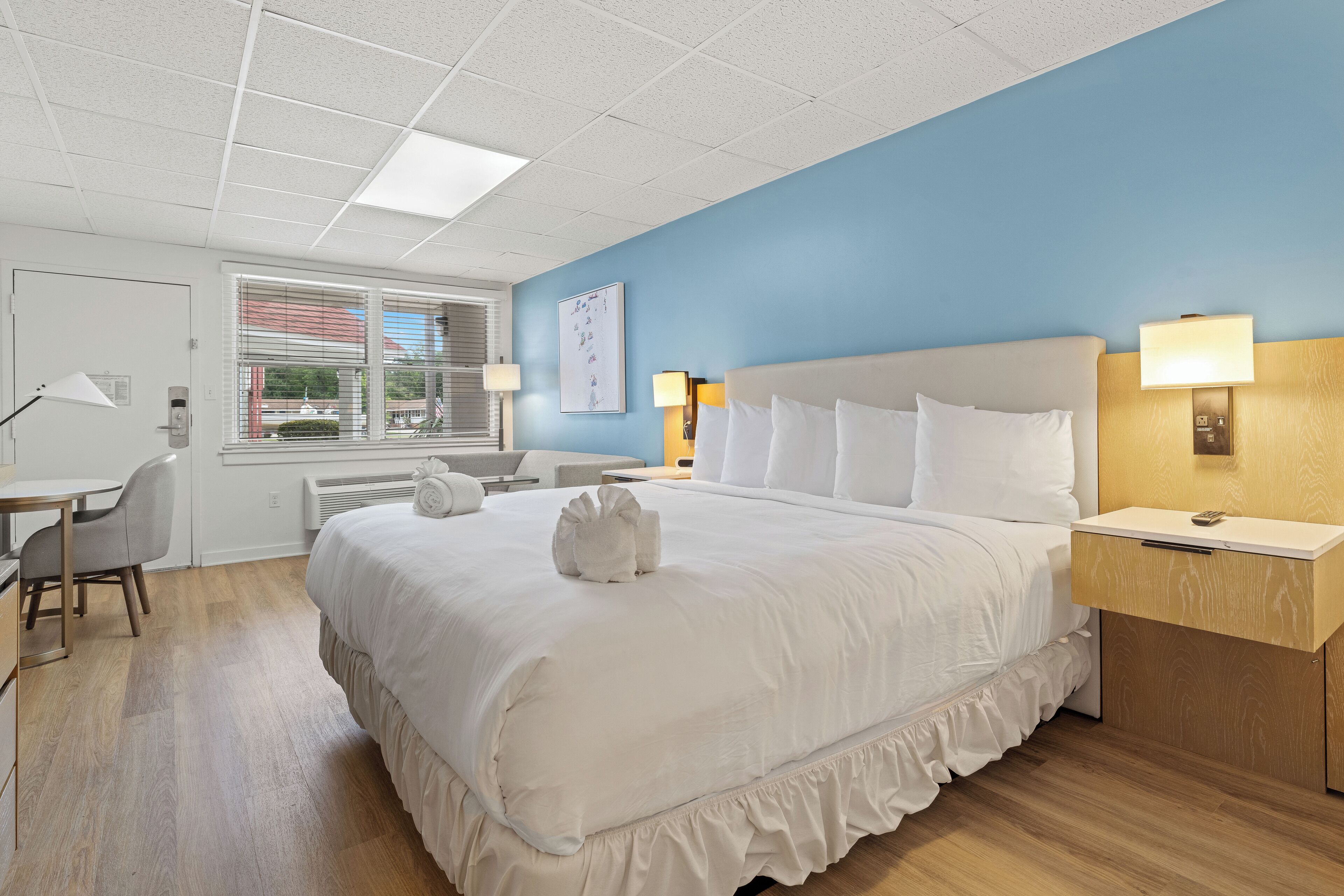 A hotel room with a large bed, bedside lamps, a desk, and a window with blinds.