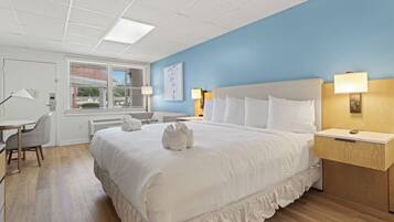 A hotel room with a large bed, bedside lamps, a desk, and a window with blinds.
