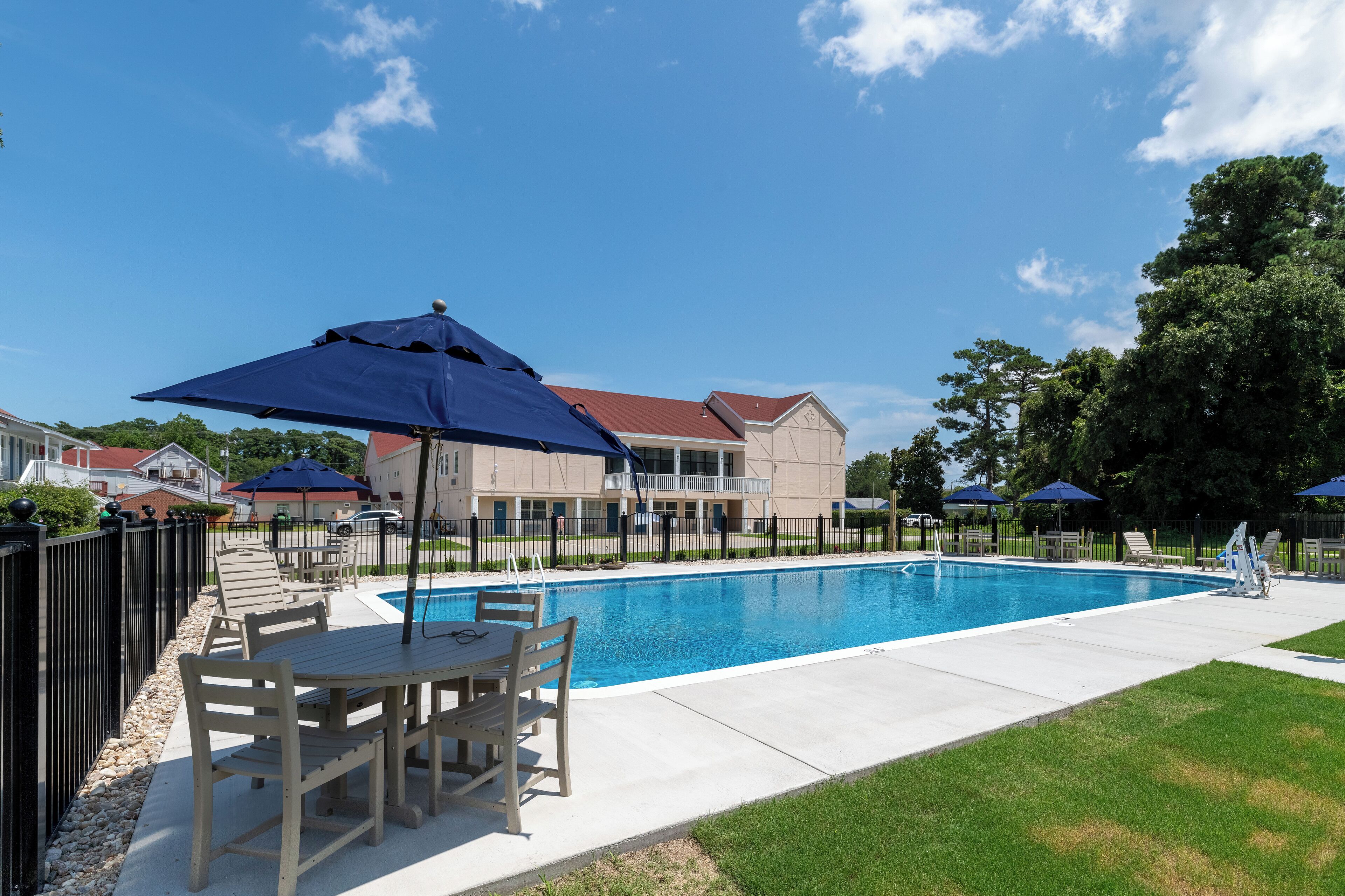 Una piscina con un'area prendisole, inclusi tavolo e sedie, e una zona relax coperta con ombrelloni.