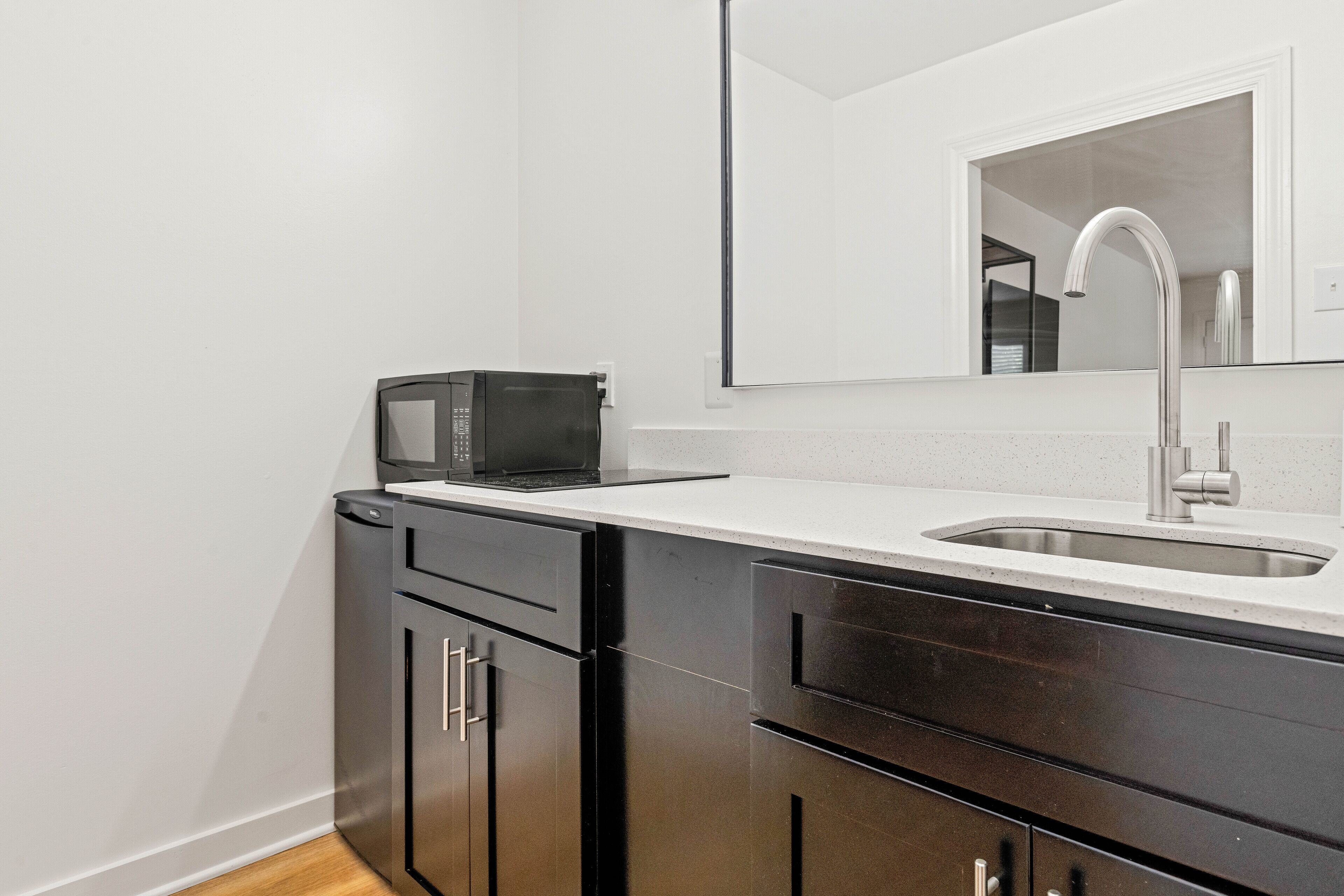 A modern kitchen with a stainless steel microwave, a sink, and dark wooden cabinets.