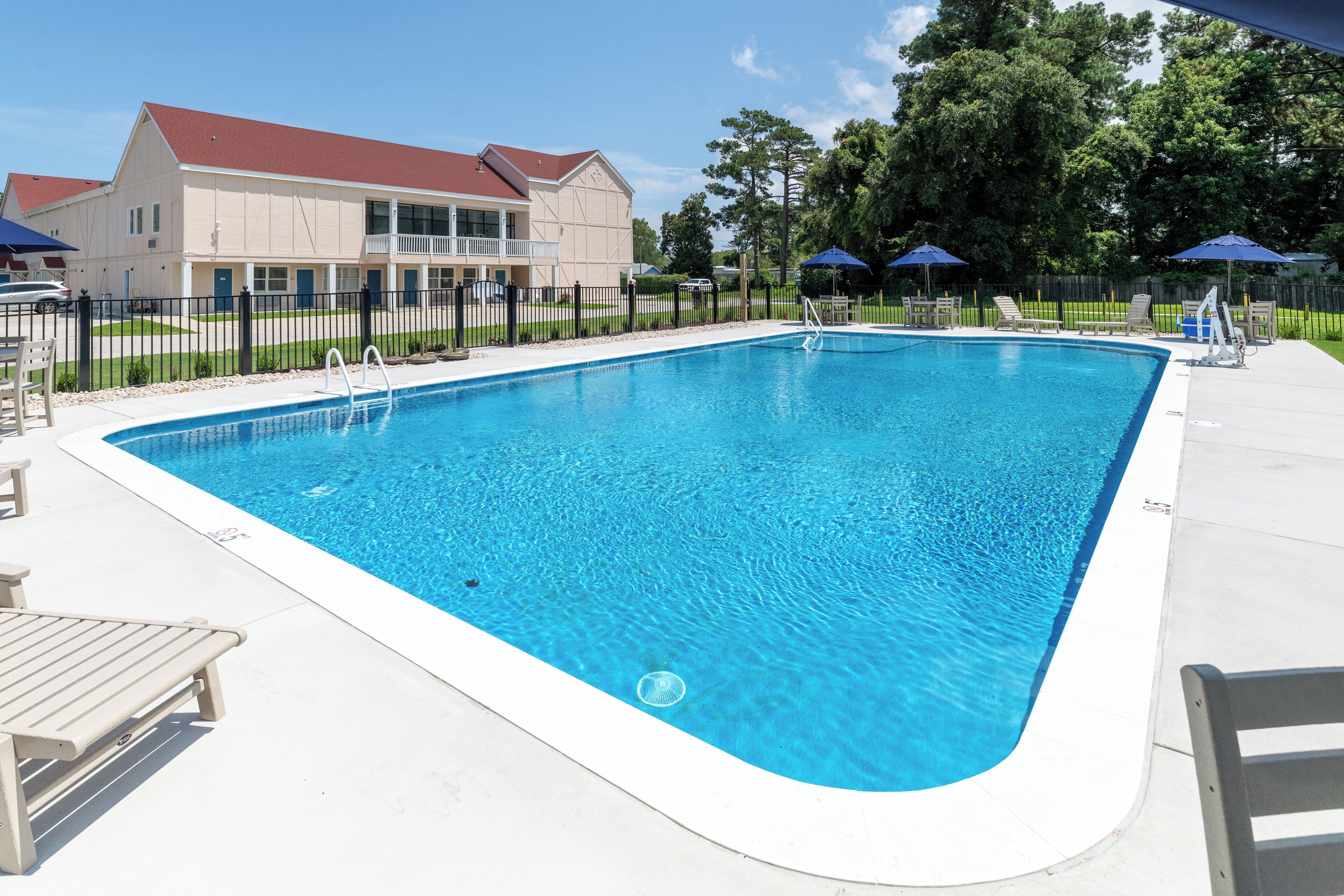 Una piscina rettangolare con acqua cristallina e bordi in legno bianco. Lungo il bordo piscina, ci sono lettini e ombrelloni.