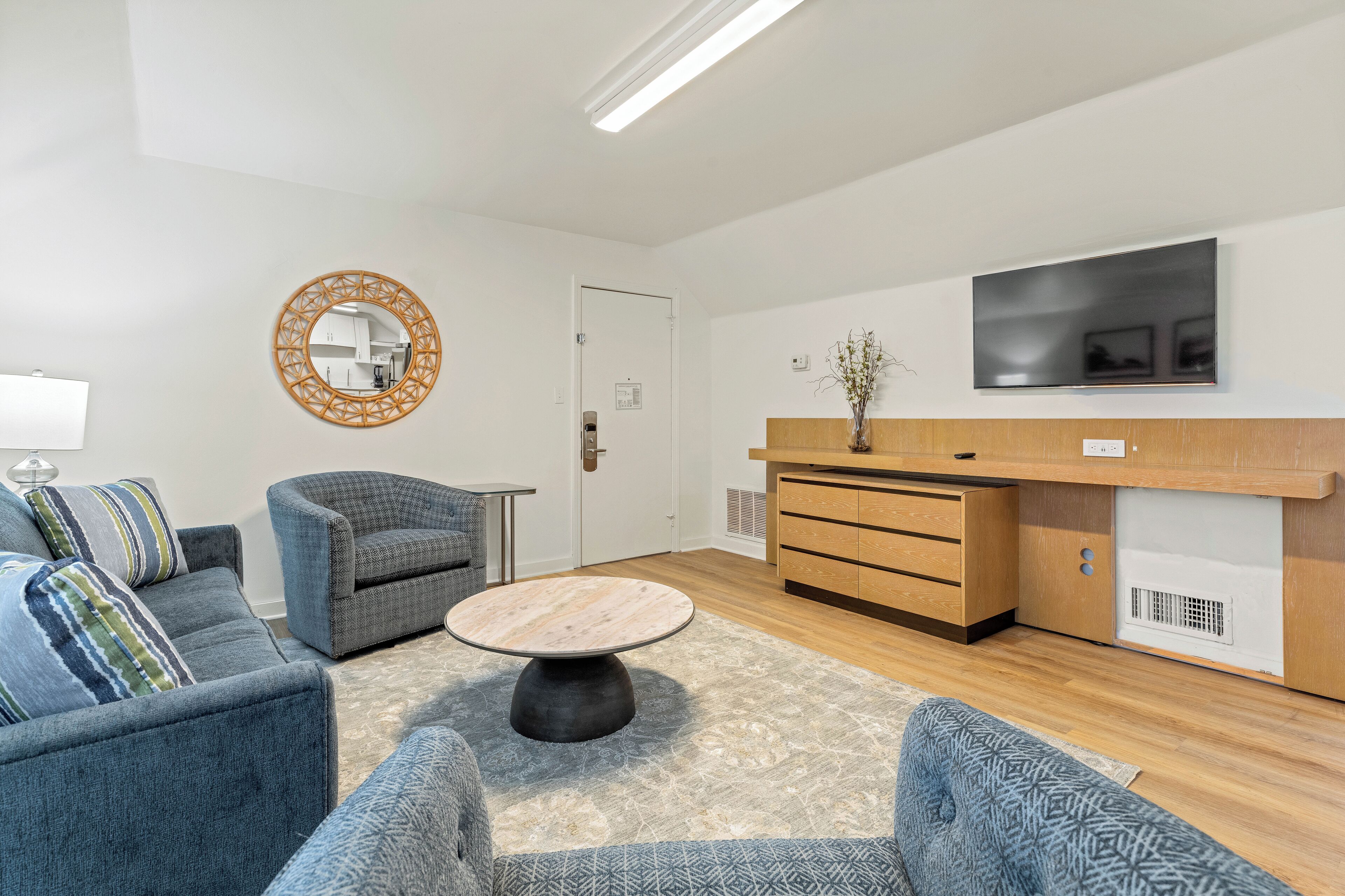 Een moderne woonkamer met een bank, fauteuil, salontafel en een aan de muur bevestigde televisie.