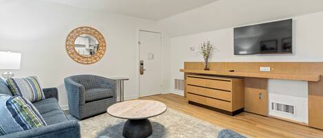 Een moderne woonkamer met een bank, fauteuil, salontafel en een aan de muur bevestigde televisie.