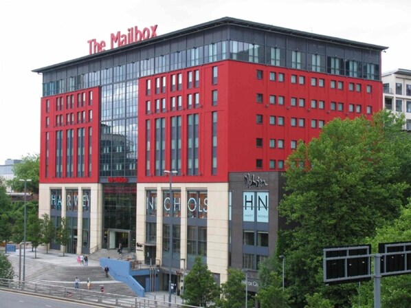 Un bâtiment moderne à la façade rouge et aux grandes fenêtres, portant l’inscription « The Mailbox ».