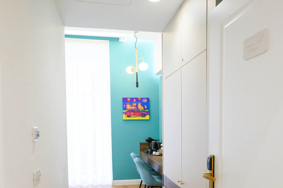 A hallway with wooden flooring, a dining area with a table and chairs, and a kitchen area with cabinets and a hanging light fixture.