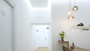 A hallway with wooden flooring, white walls, and a reception desk with a vase of flowers. - Annapoli Rooms (Naples)