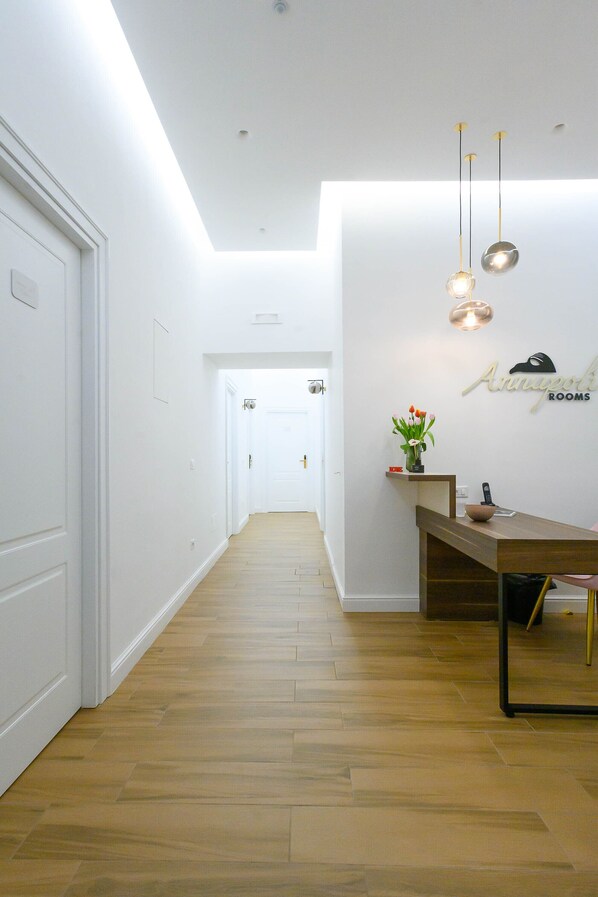 A hallway with wooden flooring, white walls, and a reception desk with a vase of flowers. - Annapoli Rooms (Naples)
