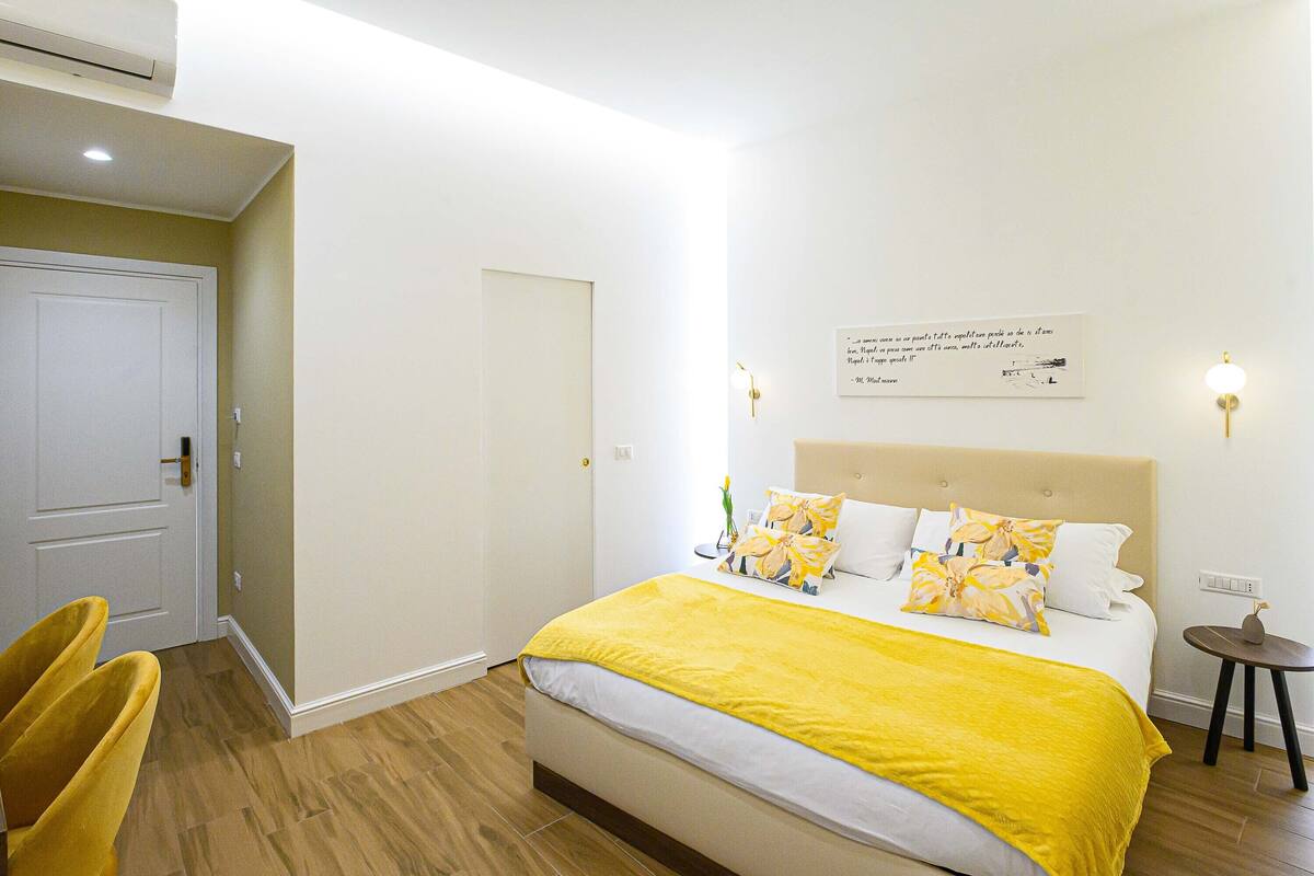 A bedroom with a bed, a bedside table, a chair, and a wall-mounted light fixture.