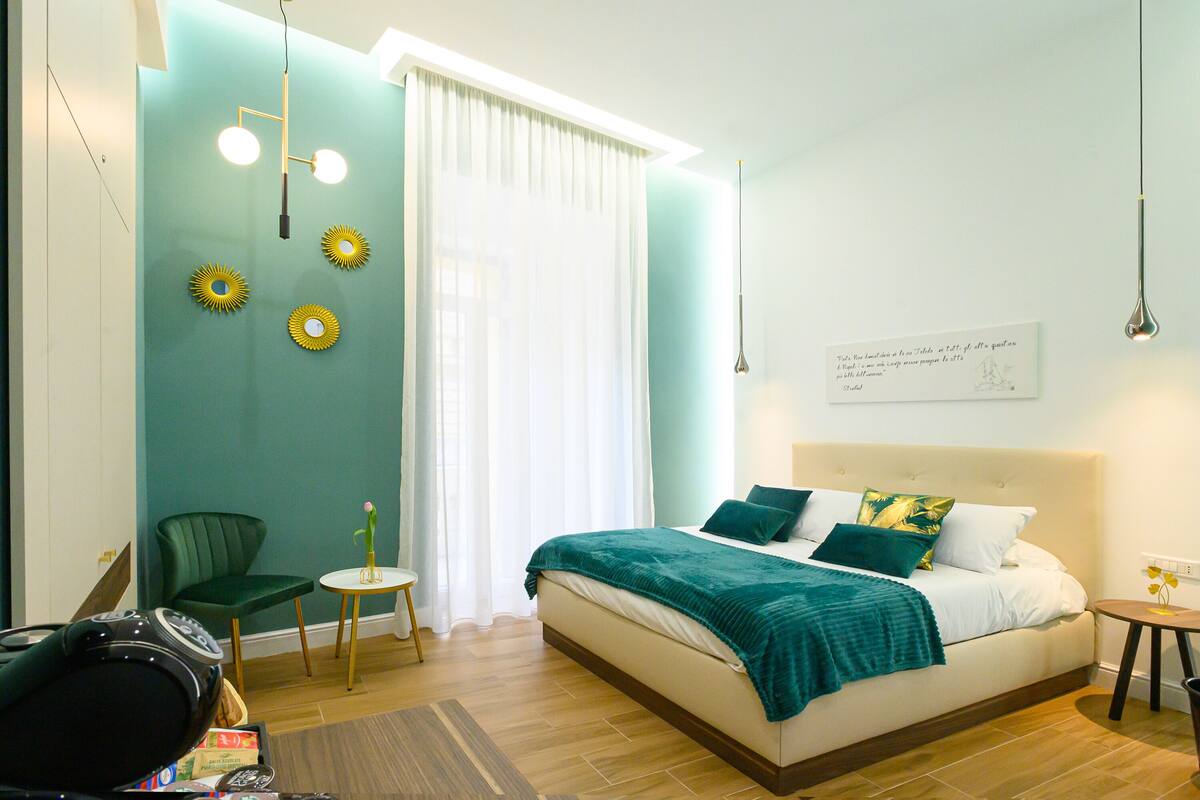 A modern bedroom with a bed, a chair, a small table, and a wall with decorative elements.