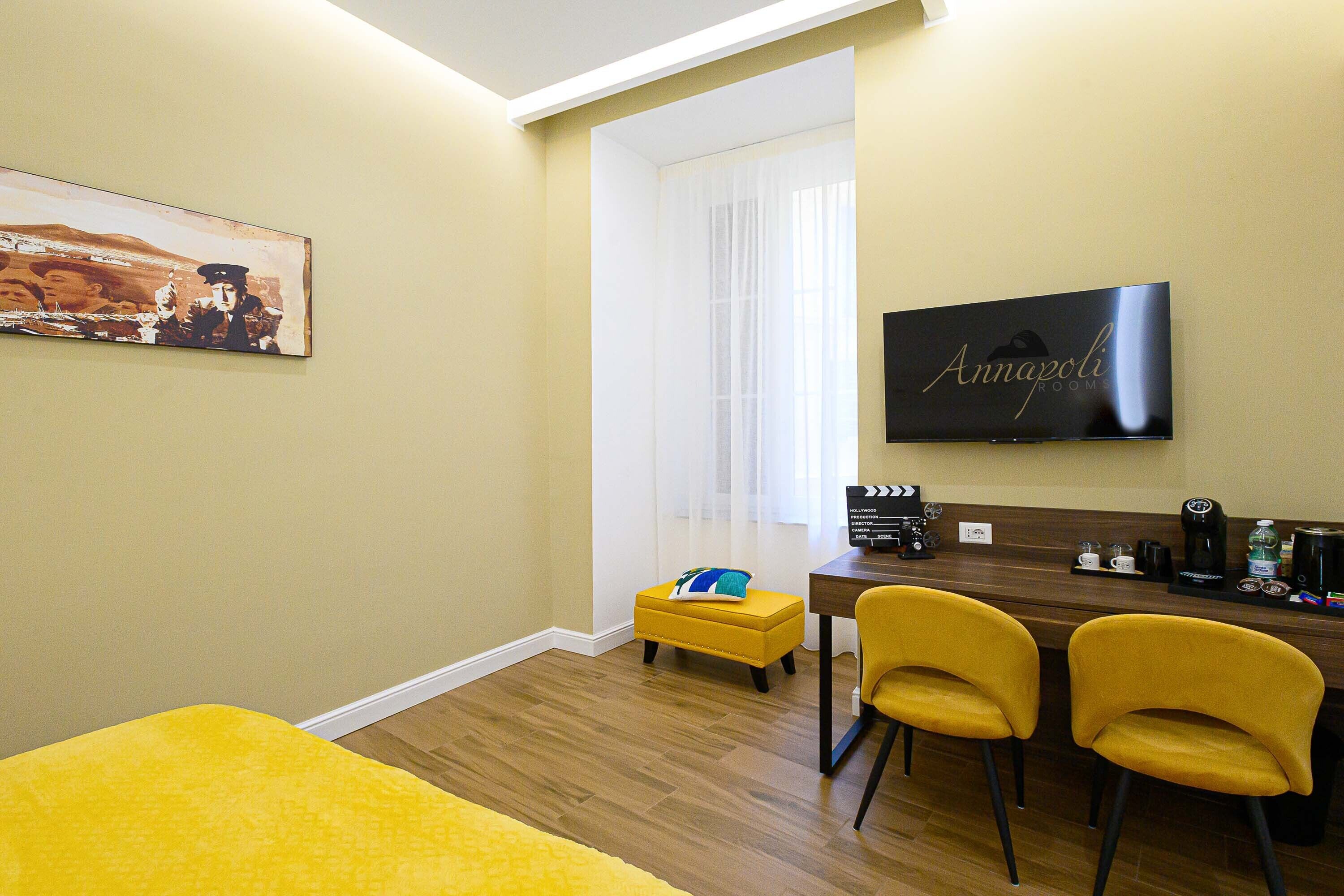 A hotel room with a bed, a desk with a chair, a television, and a painting on the wall.