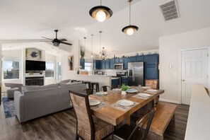 A modern kitchen with dark blue cabinets, a stainless steel refrigerator, and a dining area with a wooden table and chairs.