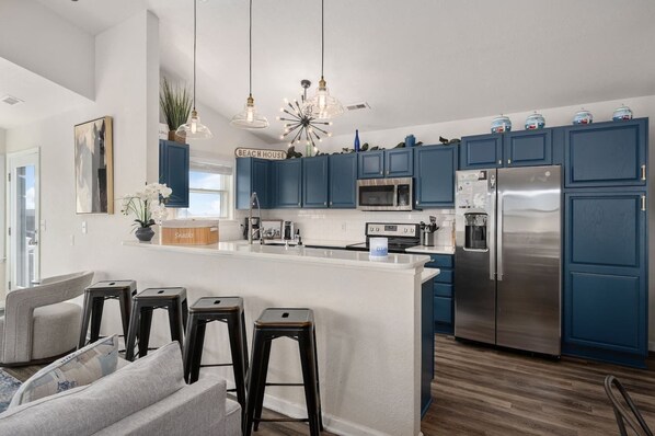 A modern kitchen with blue cabinets, a stainless steel refrigerator, and a bar area with stools.