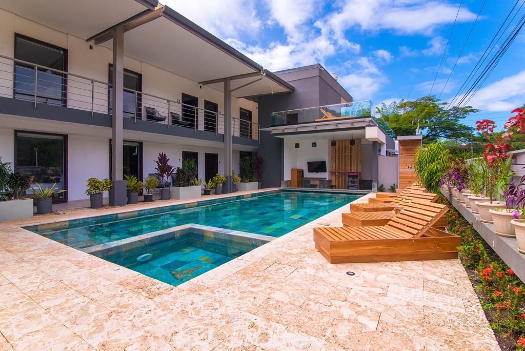 Una casa moderna con piscina, mobiliario exterior y plantas en macetas.
