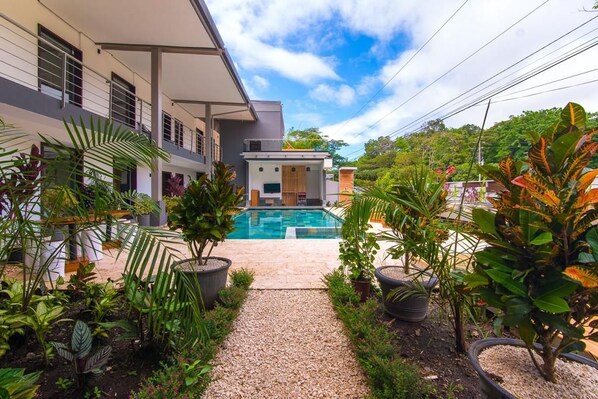A modern house with a swimming pool, surrounded by lush tropical plants and a gravel pathway. - Hotel Paradise Bay (Jacó)