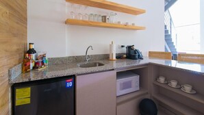 Eine kompakte Küche mit integriertem Geschirrspüler, Spüle und Mikrowelle. Über der Spüle befinden sich Regale mit Gläsern und auf der Arbeitsfläche steht eine Kaffeemaschine.