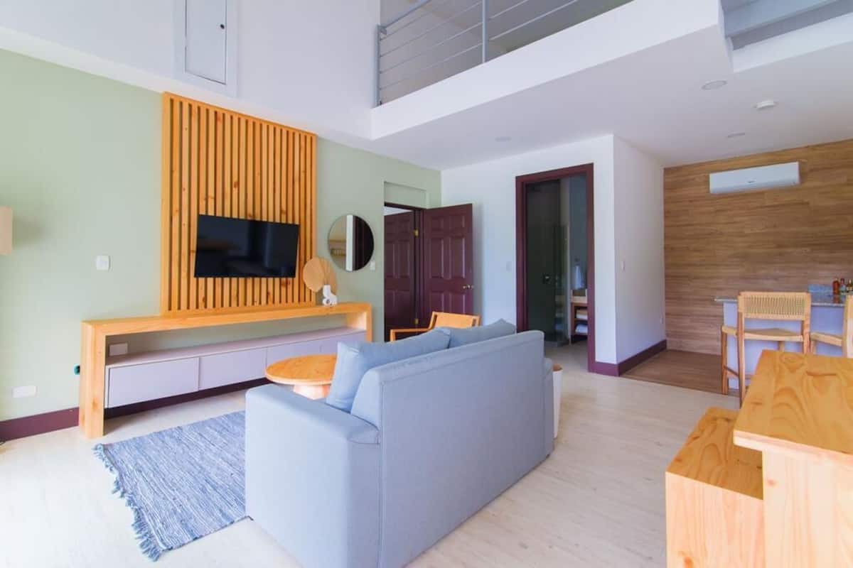 A modern living room with a sofa, TV, wooden panel wall, and a dining area with a table and chairs.