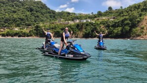 Drei Personen auf Jetskis auf ruhigem Gewässer, im Hintergrund ein bewaldeter Hügel.