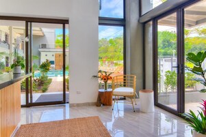 Una habitación amplia con un gran ventanal, piso de madera, una mesa redonda con una silla y una planta en maceta.