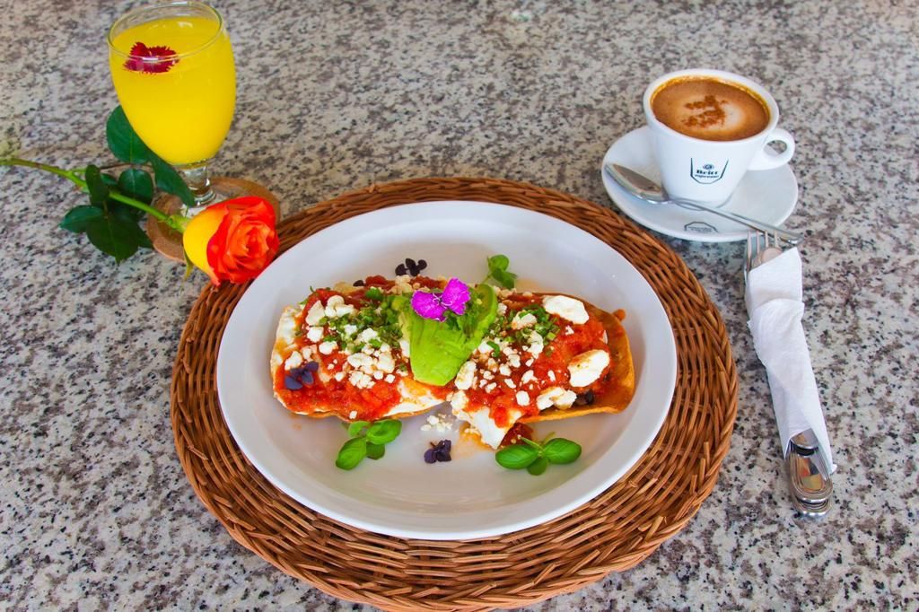 Eine Platte Enchiladas mit Belag, ein Glas Orangensaft und eine Tasse Kaffee auf einer Granitplatte.