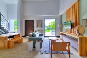 A spacious living area with a sofa, a dining table, and a TV mounted on the wall.