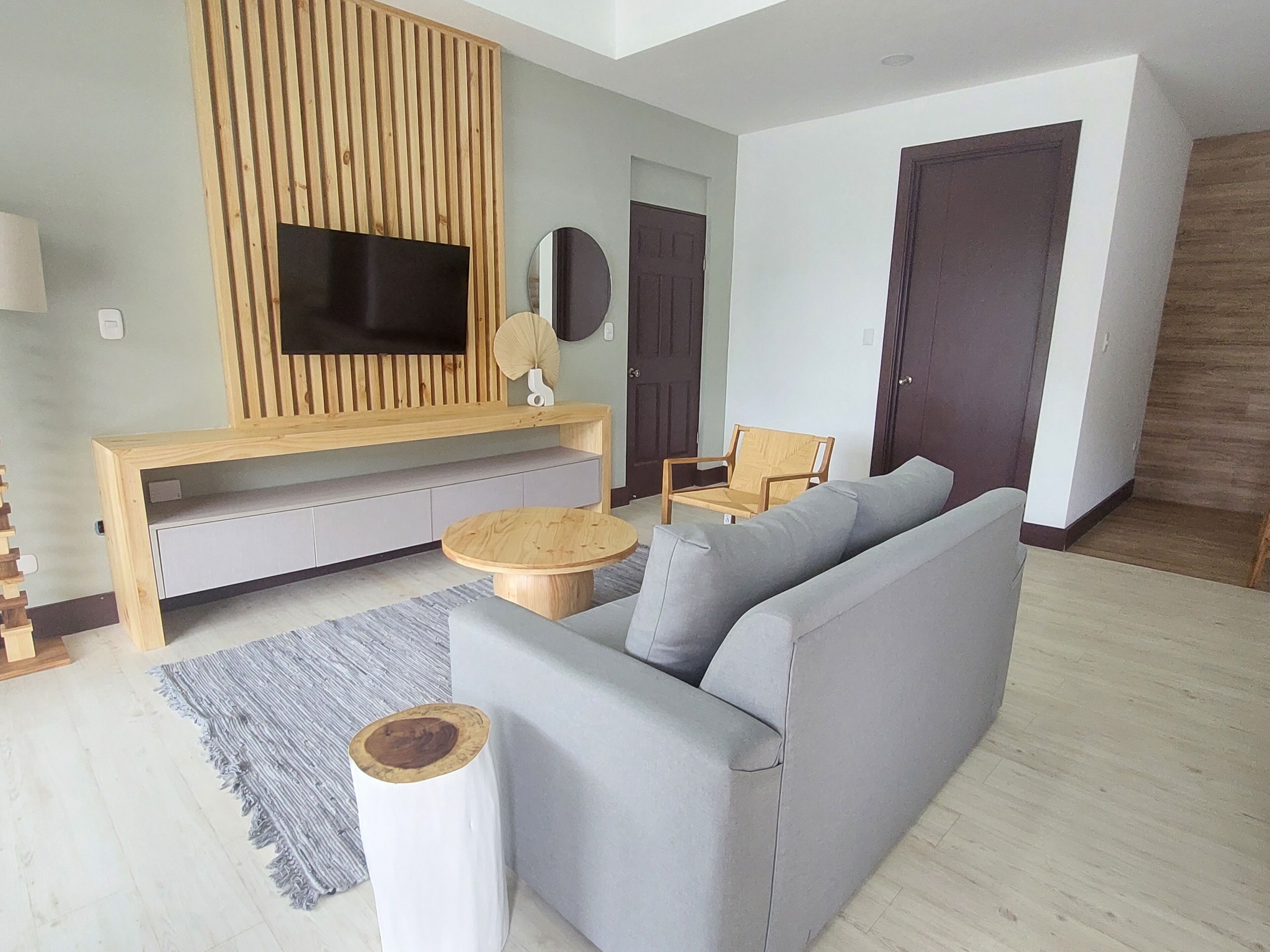 A modern living room with a grey sofa, wooden entertainment unit, and a round wooden coffee table.