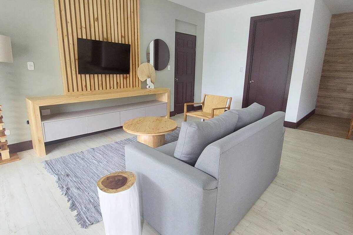 A modern living room with a grey sofa, wooden entertainment unit, and a round wooden coffee table.