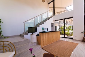 A modern interior with a reception desk, a flat-screen TV, a staircase, and a large glass door leading to an outdoor area. - Hotel Paradise Bay (Jacó)