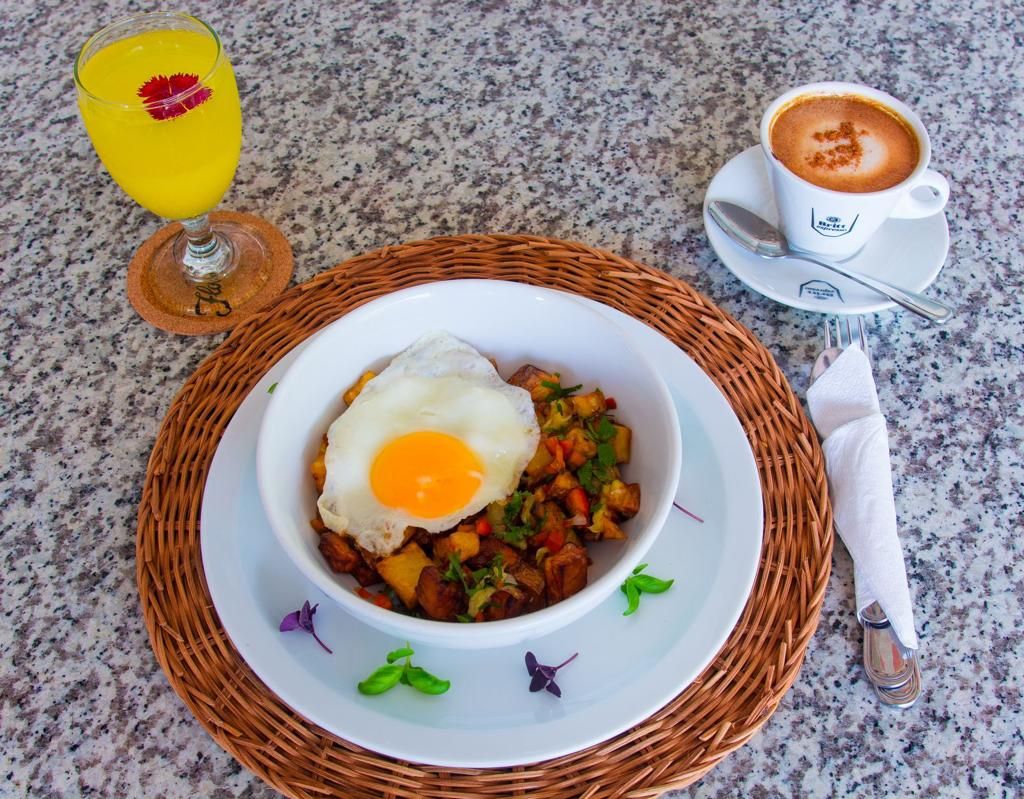 A breakfast setting with a bowl of eggs and potatoes, a glass of orange juice, and a cup of coffee on a granite countertop.