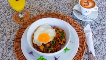 A breakfast setting with a bowl of eggs and potatoes, a glass of orange juice, and a cup of coffee on a granite countertop.