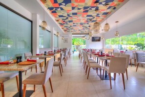 Un comedor amplio con mesas y sillas largas, ventanas grandes y un techo colorido.