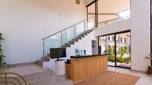 Uma área de estar moderna, com uma mesa de recepção em madeira, televisão de tela plana e escada que leva a um andar superior.