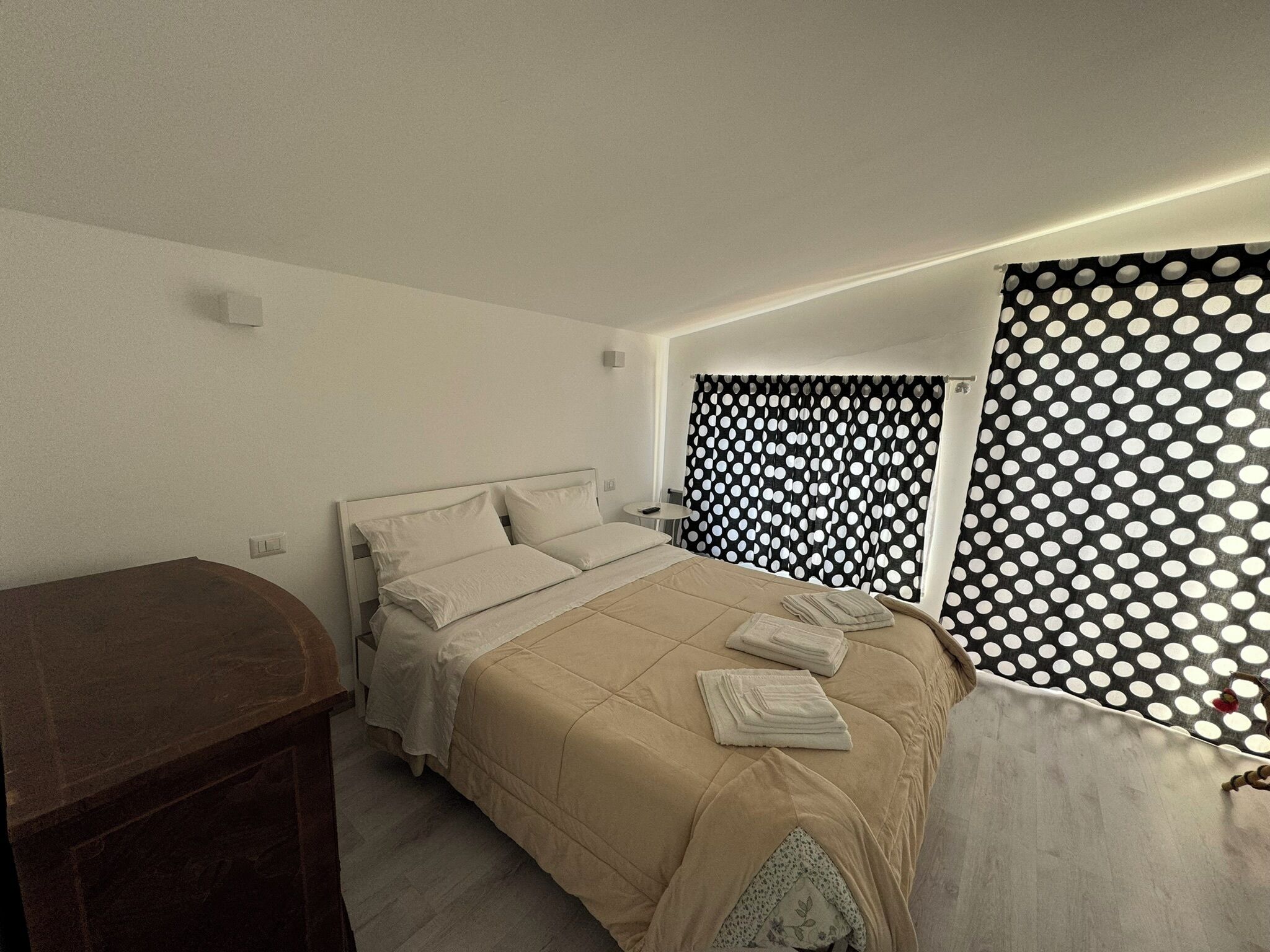 A bedroom with a bed, bedside tables, a mirror, and a polka dot curtain.