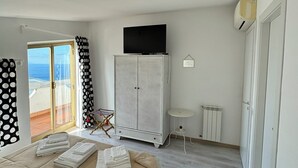 A hotel room with a bed, a wardrobe, a television, a radiator, and a view of the sea through a sliding door. - Villa Sotto le Stelle for a relaxing holiday with a view of the Aeolian Islands (Orto Liuzzo)