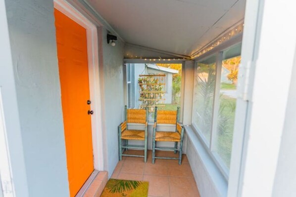 A narrow hallway with an orange door, two wicker chairs, a small table, and a plant. - The Orange Door - Coastal Escape (Stuart)