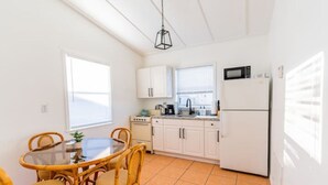 A compact kitchen with white cabinets, a microwave, and a dishwasher. There is a dining table with chairs and a hanging light fixture. - The Orange Door - Coastal Escape (Stuart)