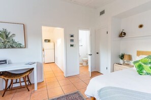 A bedroom with a bed, a desk, and a chair. There is a door leading to another room. - The Orange Door - Coastal Escape (Stuart)